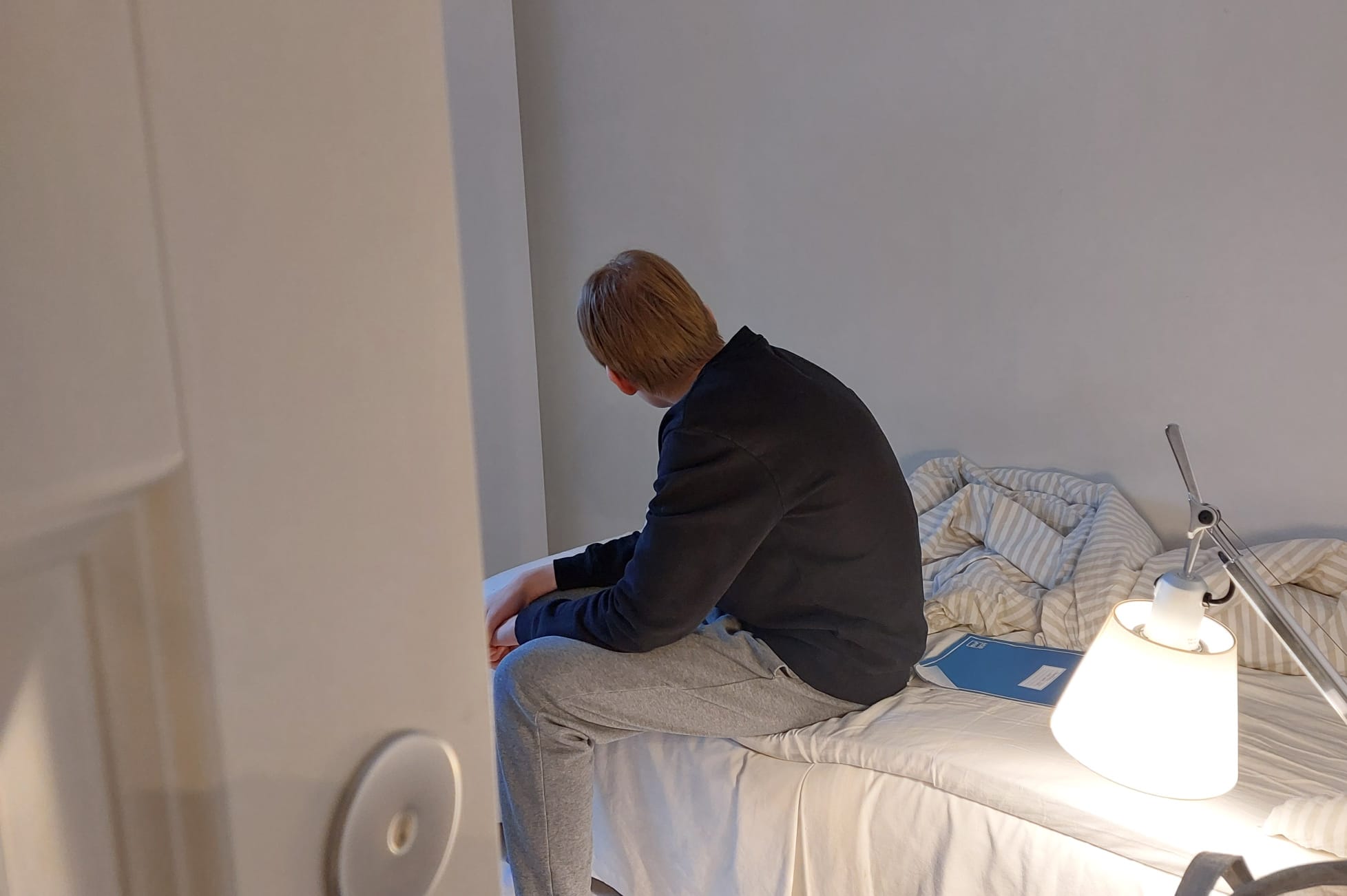 Nuori poika istuu sängyn reunalla pää käännettynä pois päin kamerasta.