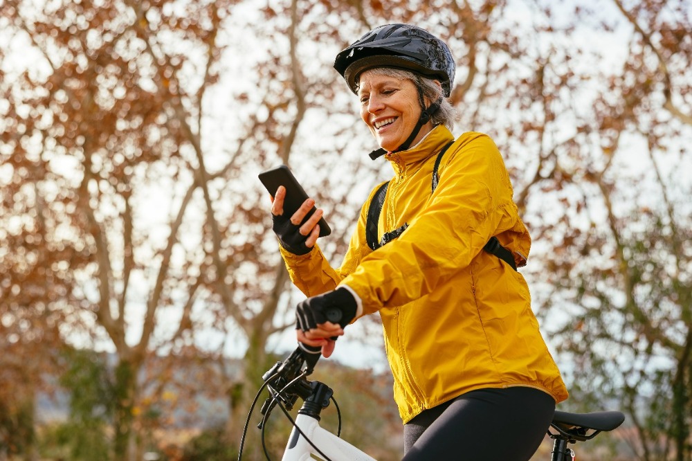 Nainen on pyöräilemässä ja katsoo hymyillen puhelintaan.