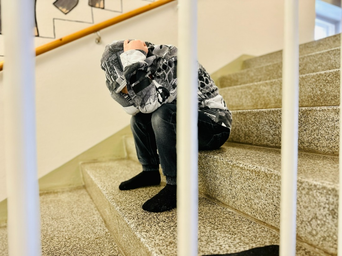 Lapsi istuu portaissa nojaa polviin huppu päässä